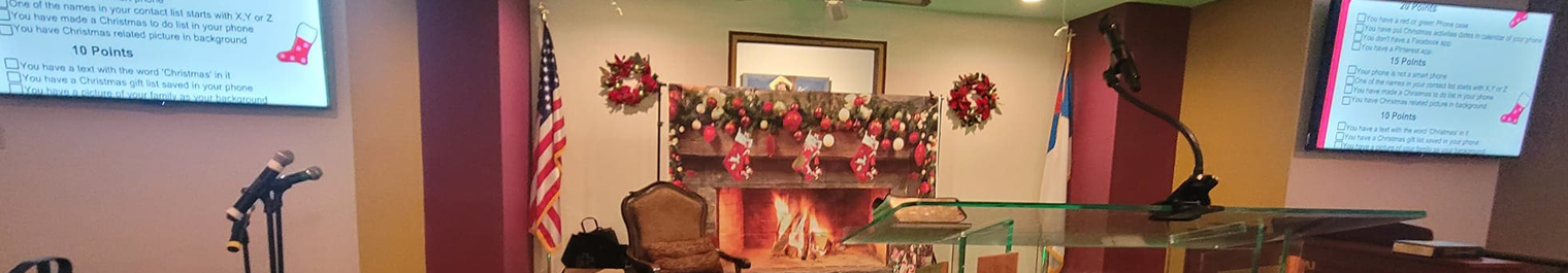 Church podium area with glass lectern, microphone, and holiday fireplace with stockings and wreaths; American flag on left and another flag on right.